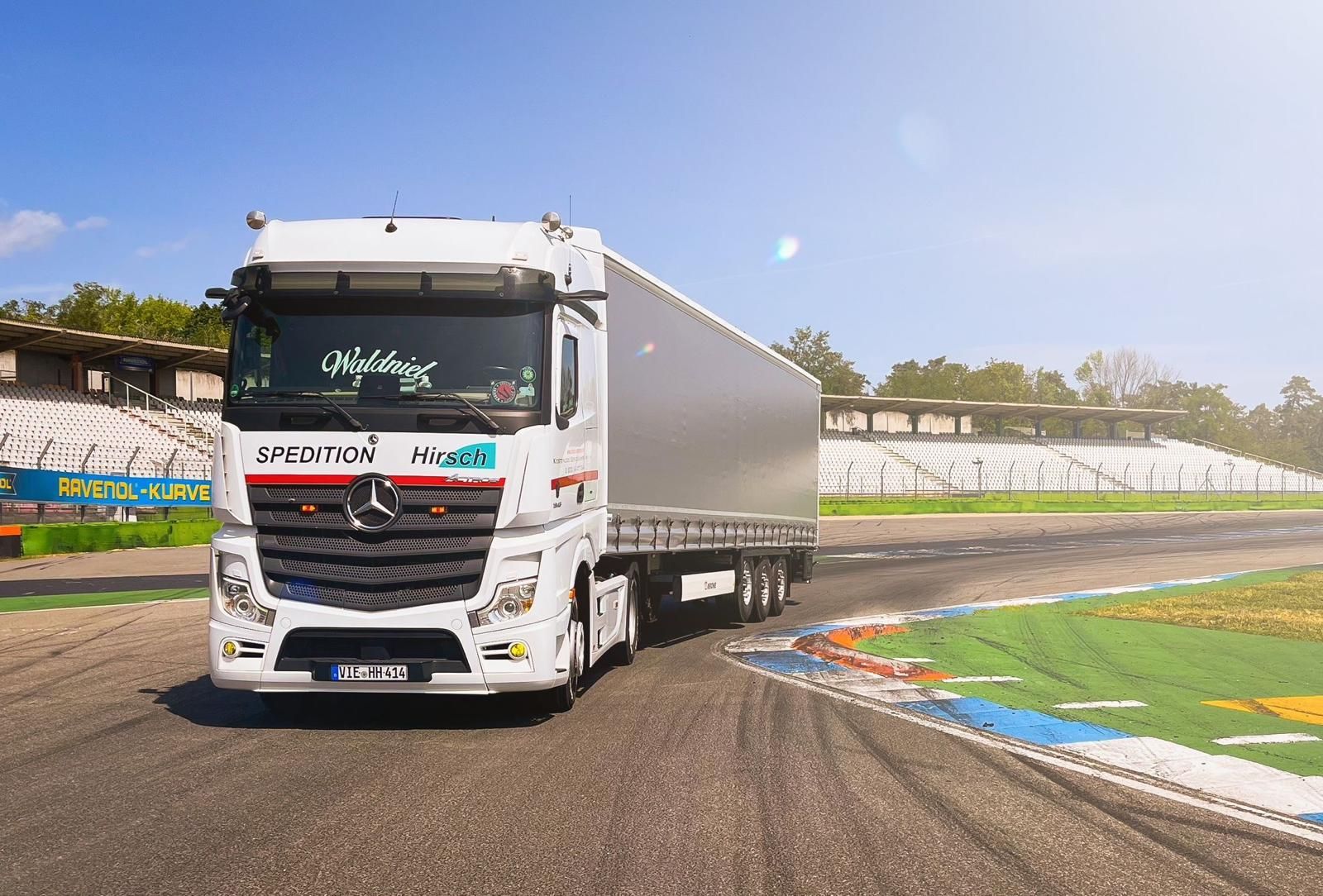 Weißer Sattelschlepper auf einer Rennstrecke mit grauem Anhänger, blauer Himmel.