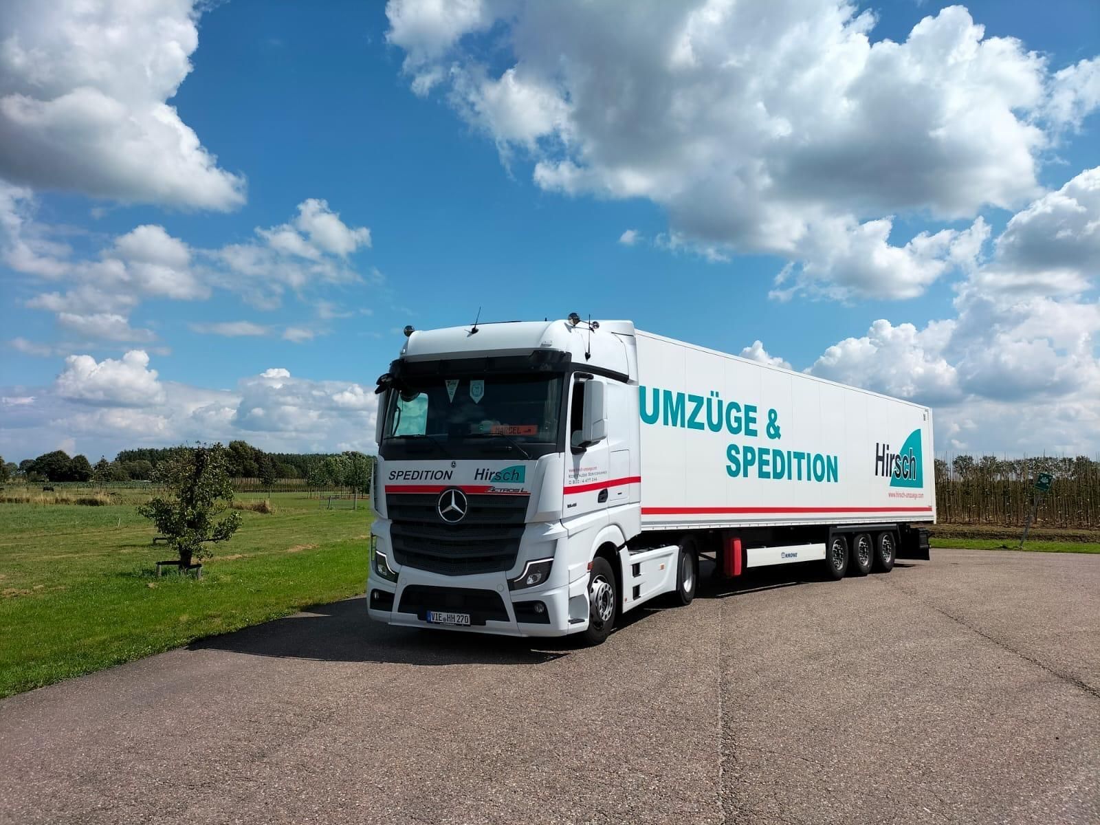 Weißer Umzugswagen auf Asphalt, mit der Aufschrift „Umzüge & Spedition“ vor blauem Himmel mit Wolken.