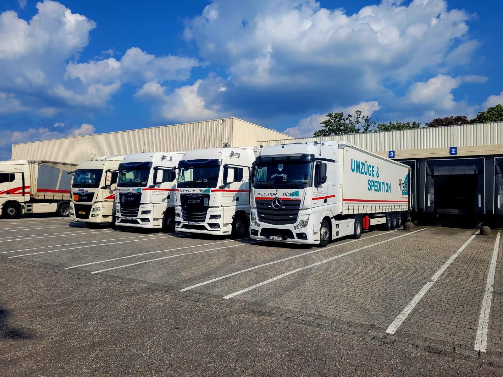 Unter einem teilweise bewölkten Himmel parken Lastwagen in einem Ladebereich.