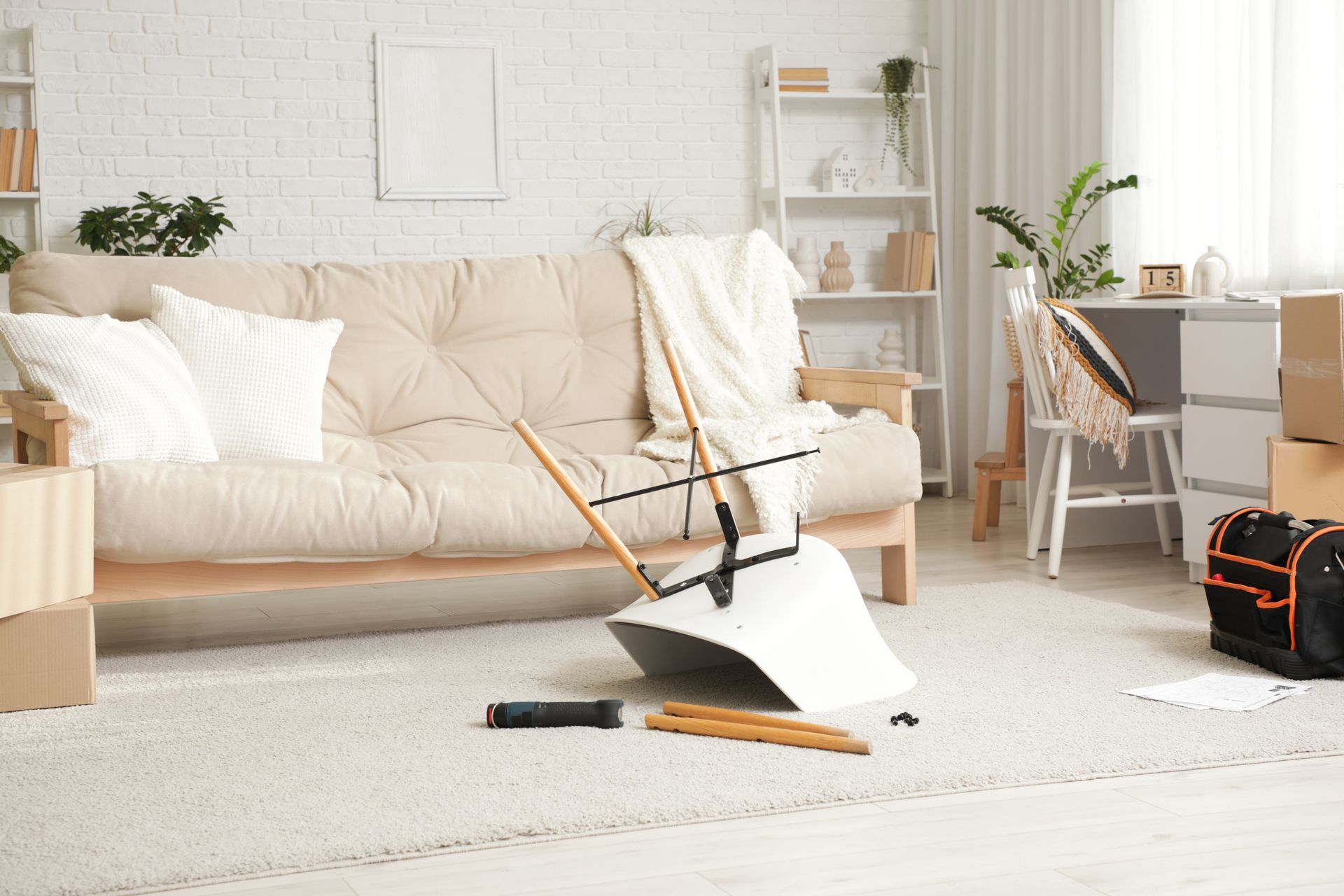 Une pièce en désordre avec un balai démonté, un futon et des cartons de déménagement.