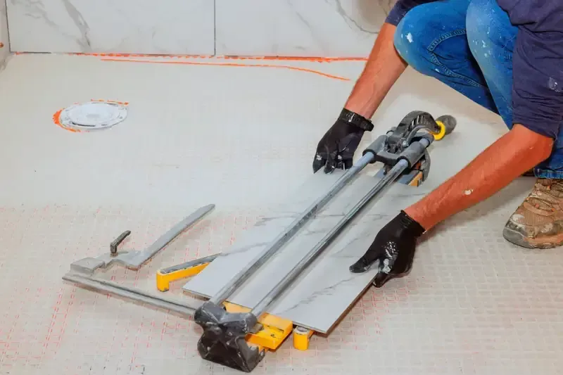 Persona cortando baldosas con un cortador de baldosas manual en un baño, usando guantes.