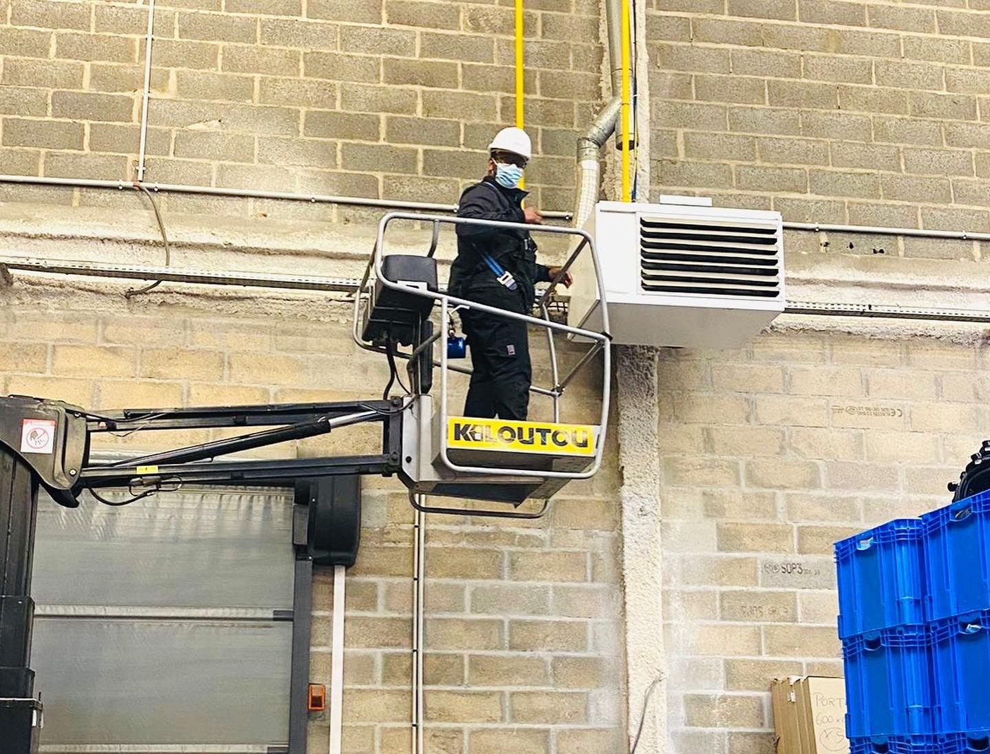 Un ouvrier se tient sur une plateforme élévatrice, travaillant près d'une unité de climatisation.