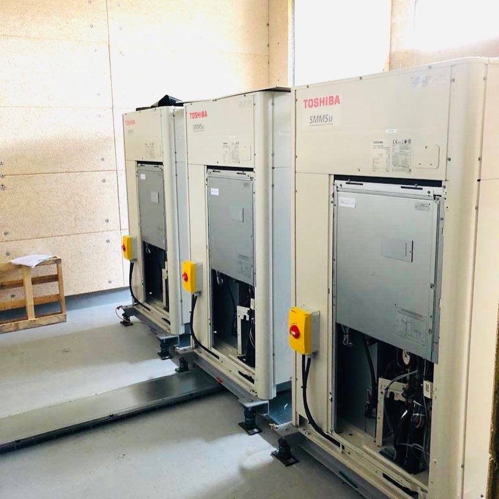 Trois unités extérieures de climatisation Toshiba sont alignées à l'intérieur d'un local technique.