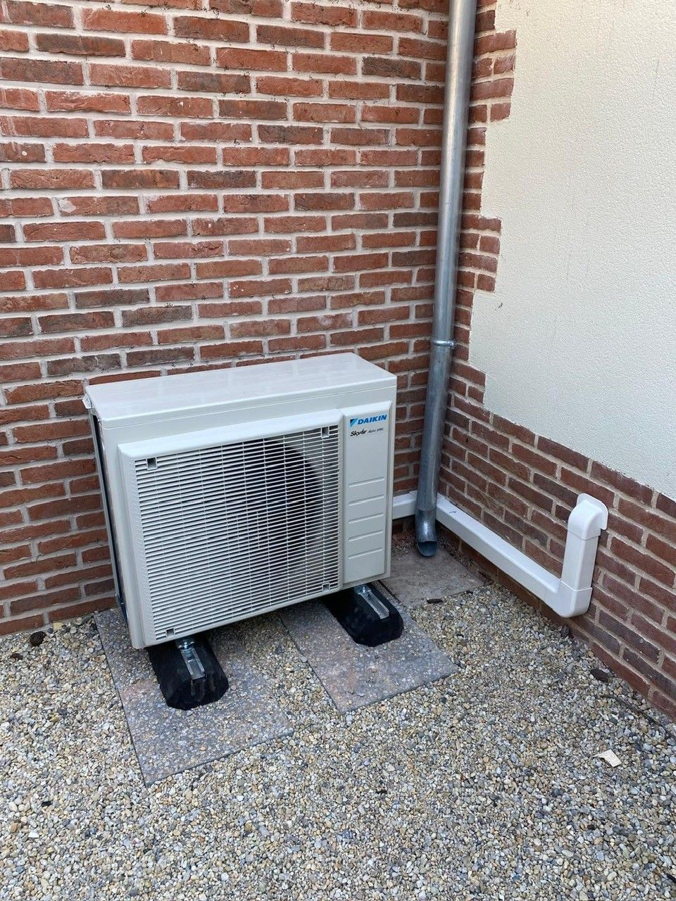 Une unité de pompe à chaleur extérieure contre un mur de briques rouges.