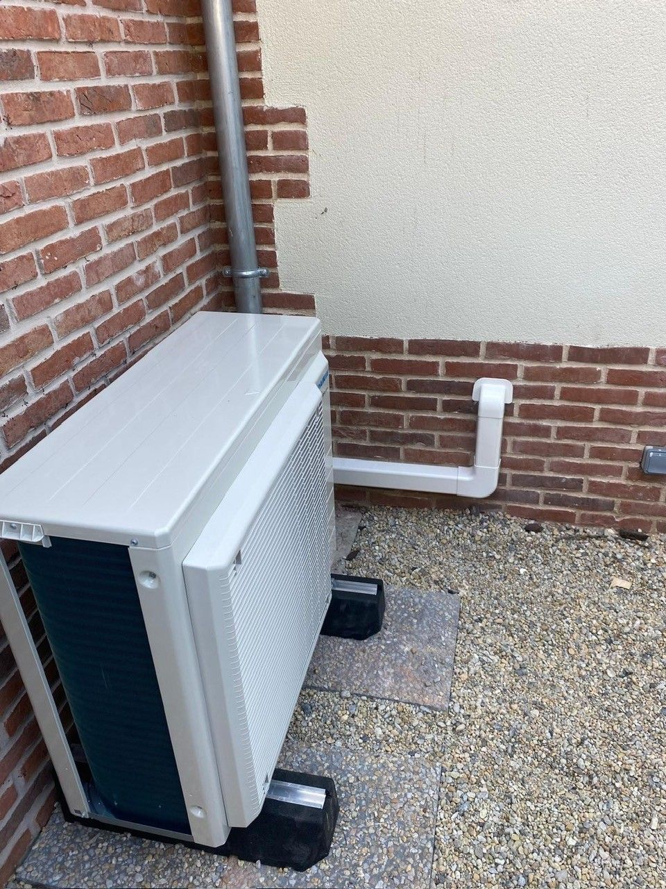 Une unité de pompe à chaleur extérieure est installée contre un mur extérieur en briques et en stuc.