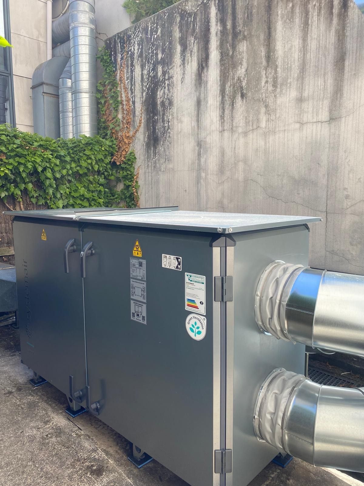 Une unité de climatisation industrielle grise est installée à l'extérieur, adossée à un mur en béton.