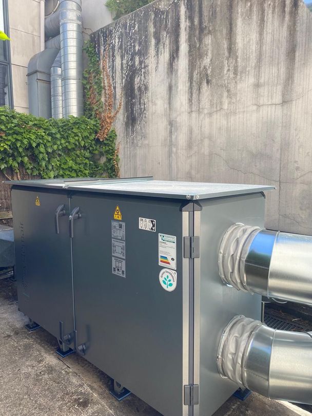 Une unité de climatisation industrielle grise est installée à l'extérieur, adossée à un mur en béton.
