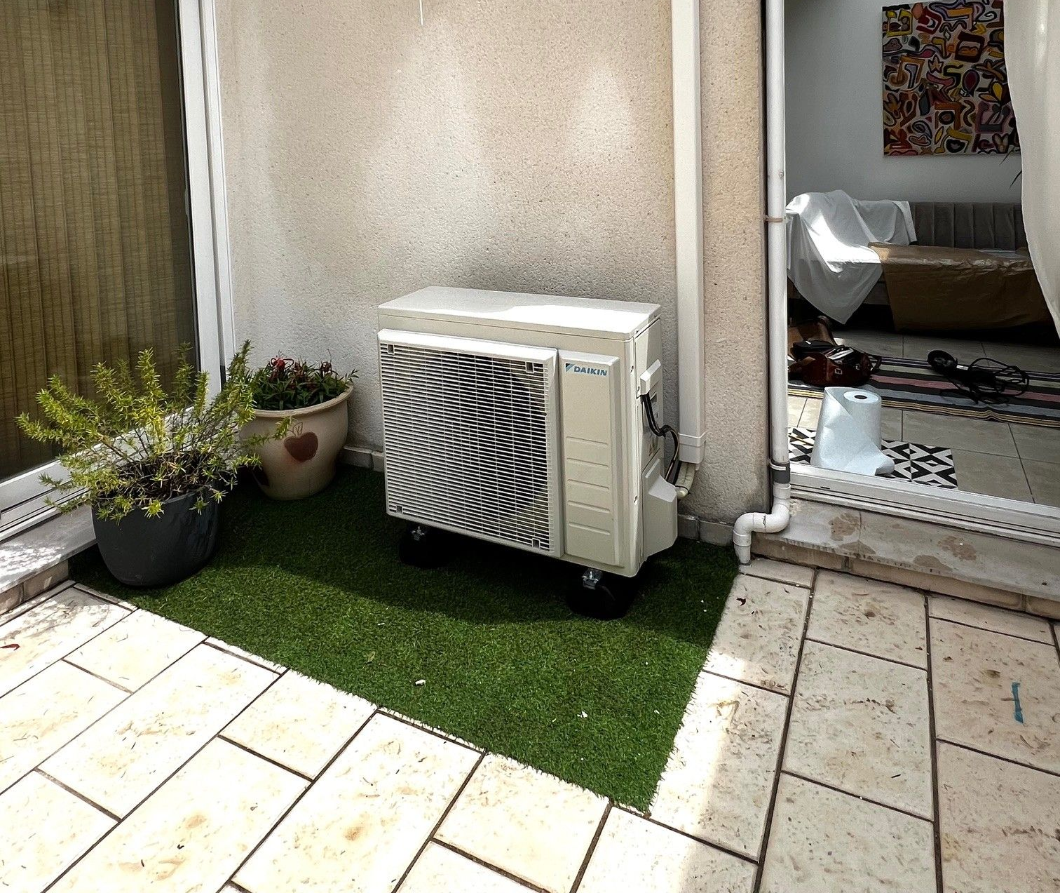 Un coin de terrasse est aménagé avec un climatiseur sur du gazon artificiel.
