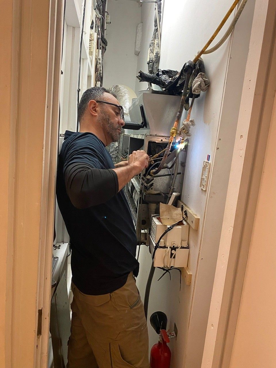 Une personne effectue des réparations sur le câblage électrique à l'intérieur d'un placard technique étroit.