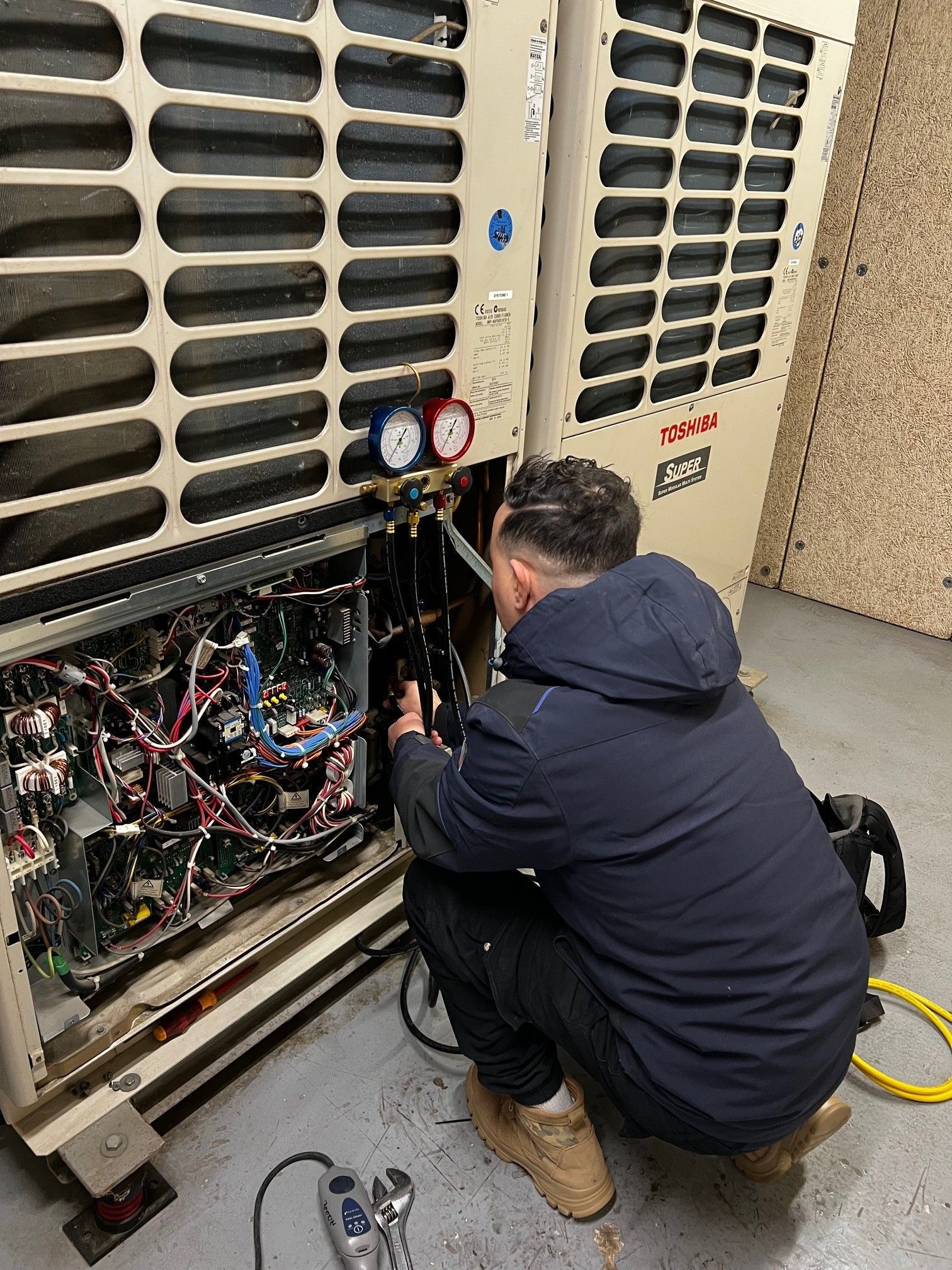 Un technicien utilise un manomètre pour entretenir une unité de climatisation industrielle.