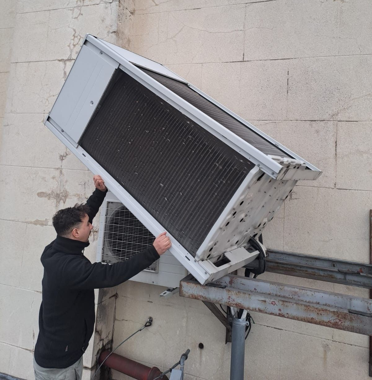 Une personne soulève une grande unité de climatisation.