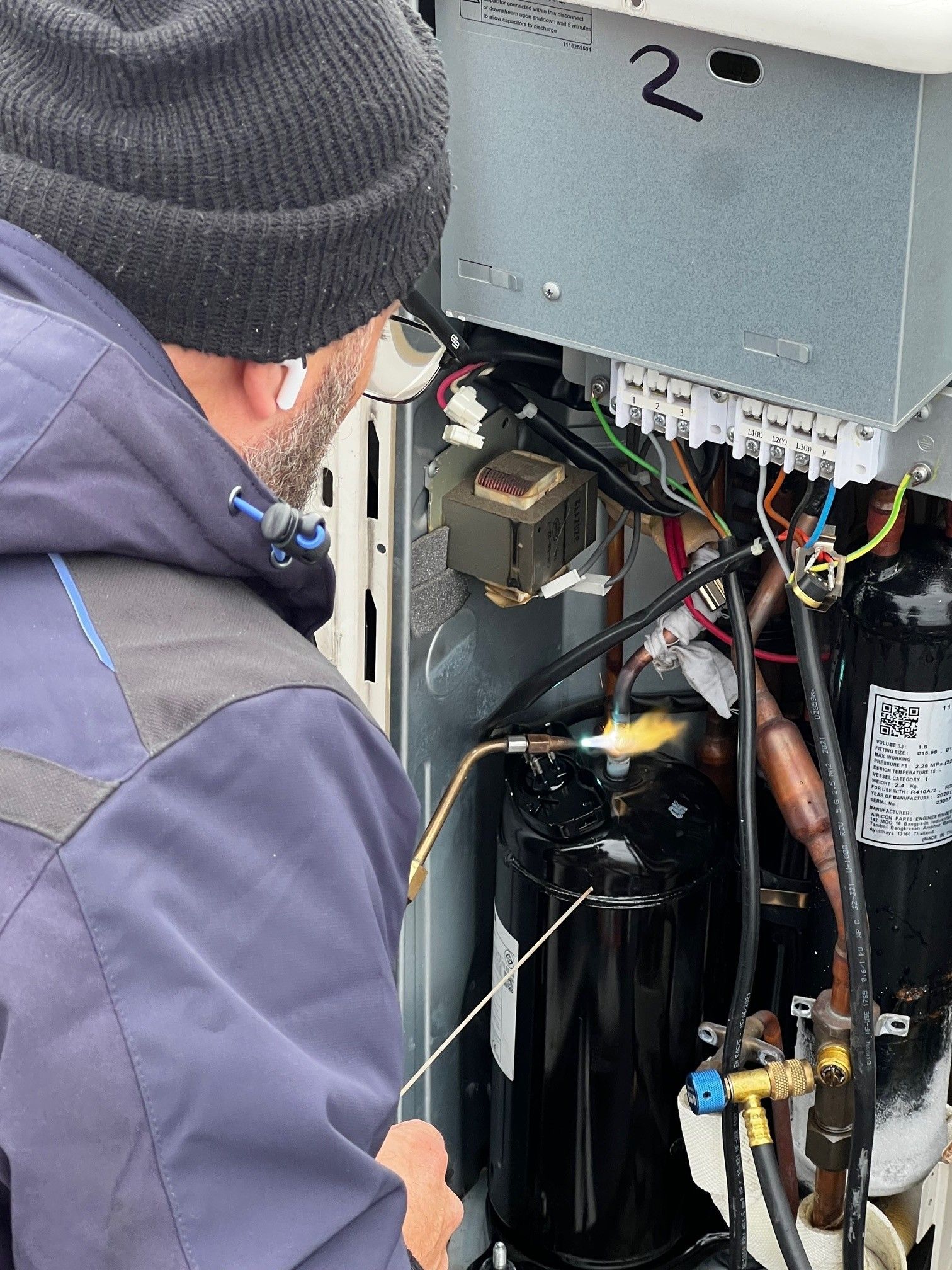 Un technicien utilise un chalumeau pour souder un tuyau de cuivre à l'intérieur de l'armoire d'une unité CVC industrielle.