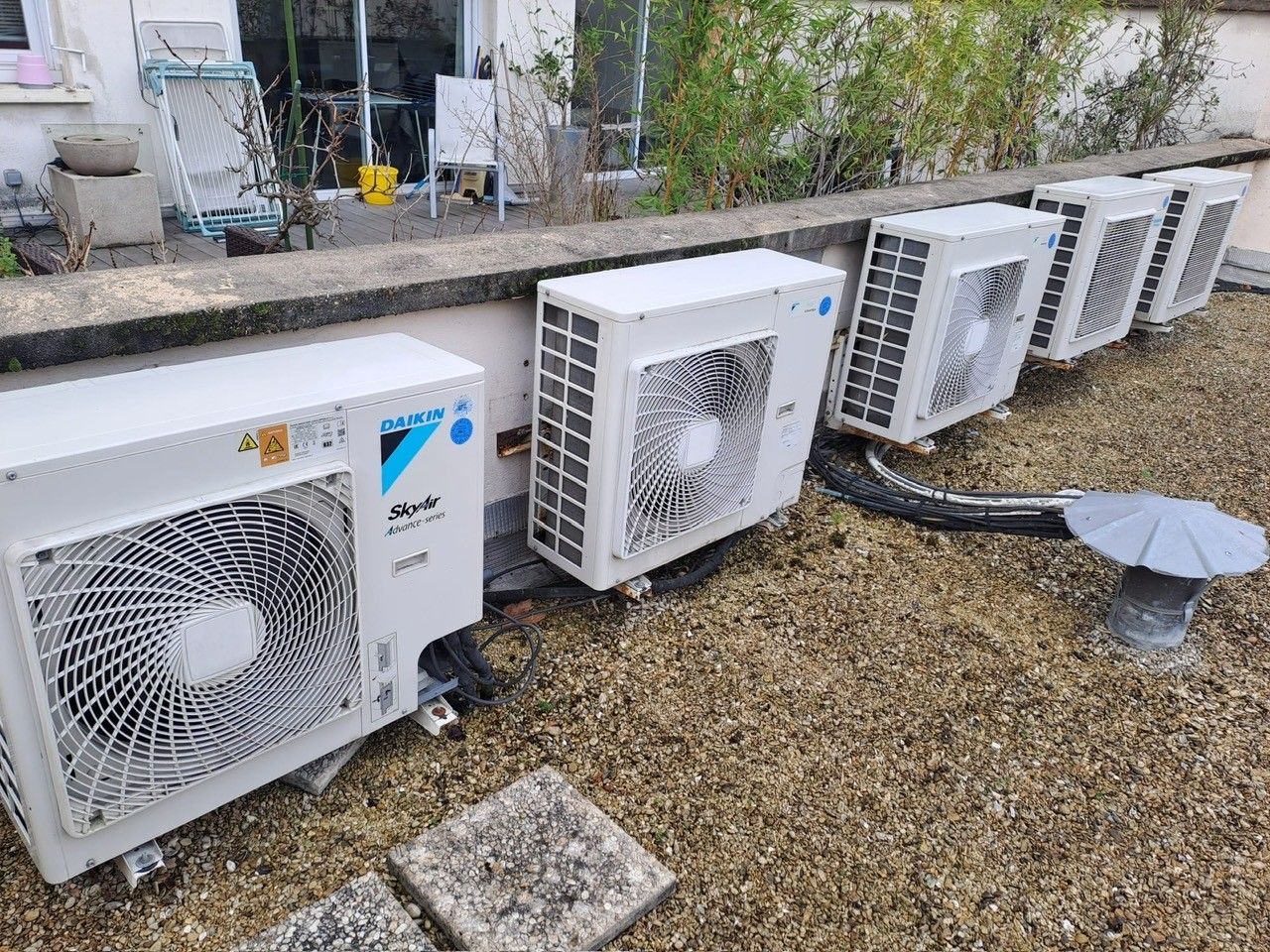 Une rangée d'unités de climatisation extérieures blanches alignées contre un muret.