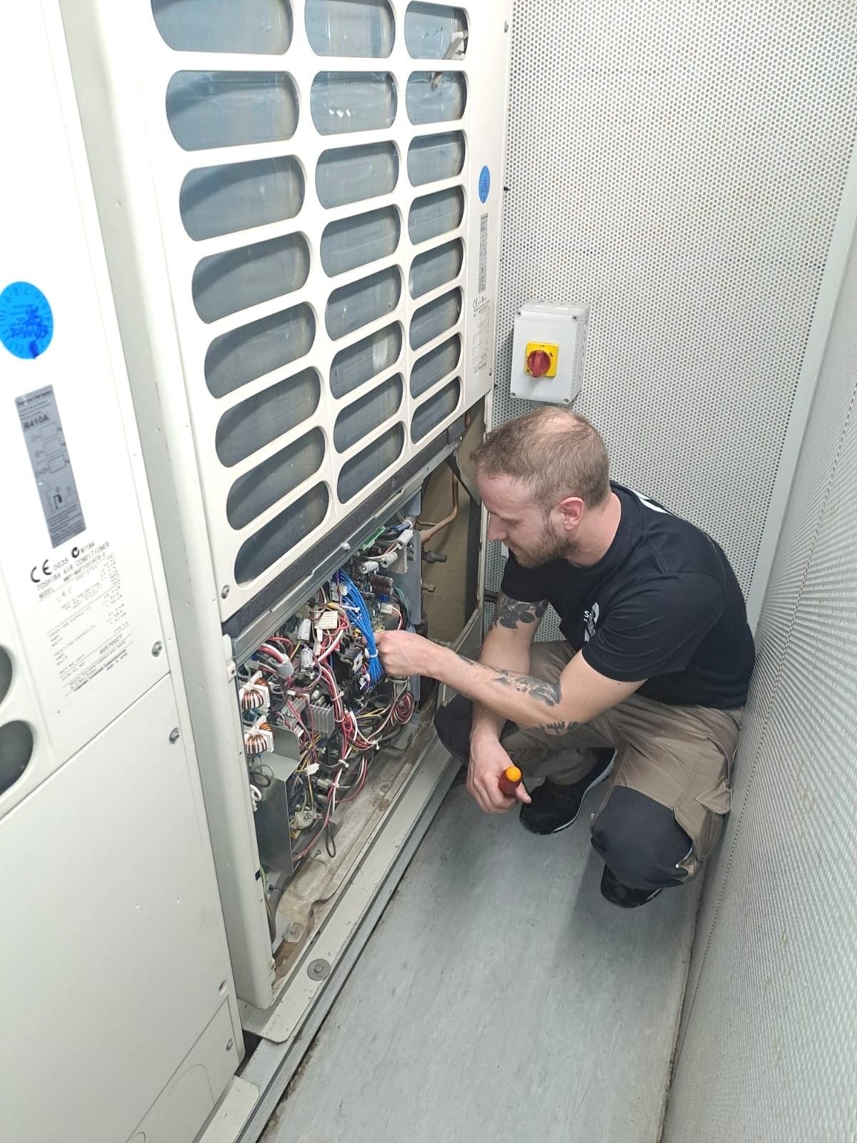 Un technicien utilise des outils pour réparer le panneau électrique ouvert d'une unité de climatisation industrielle.