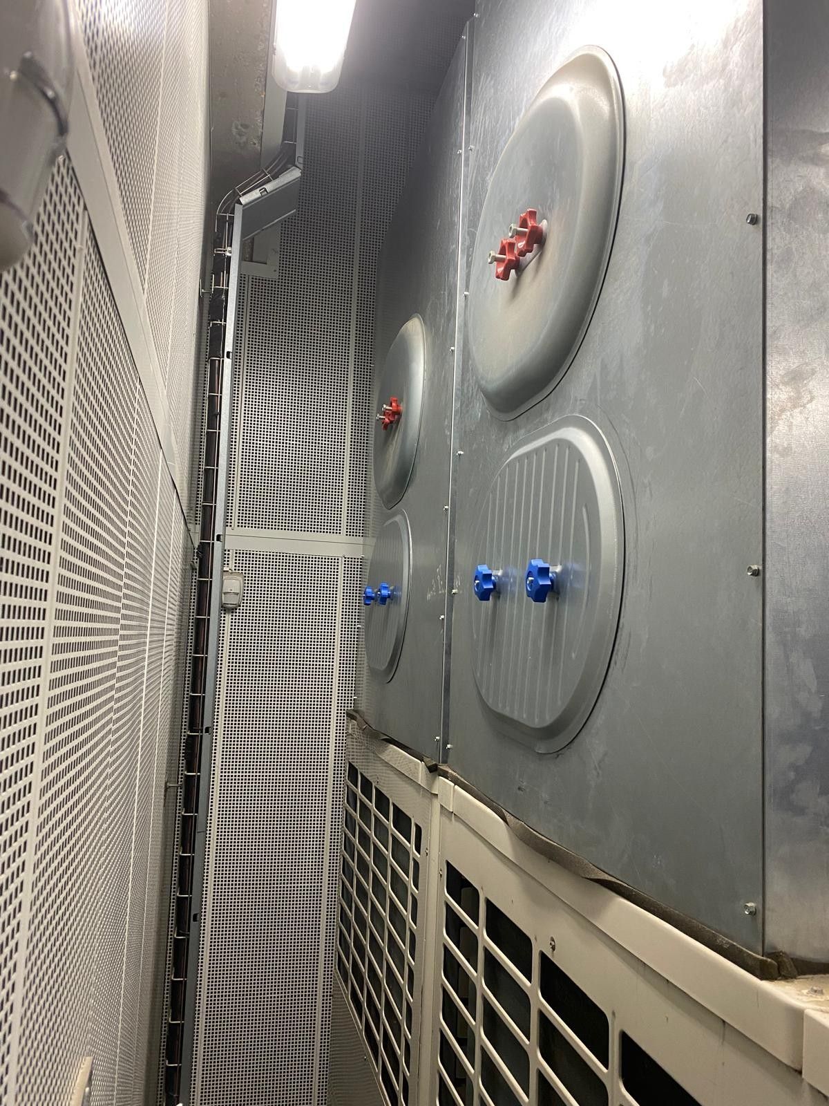 Des panneaux métalliques industriels avec des vannes rouges et bleues à droite et des grilles à gauche.