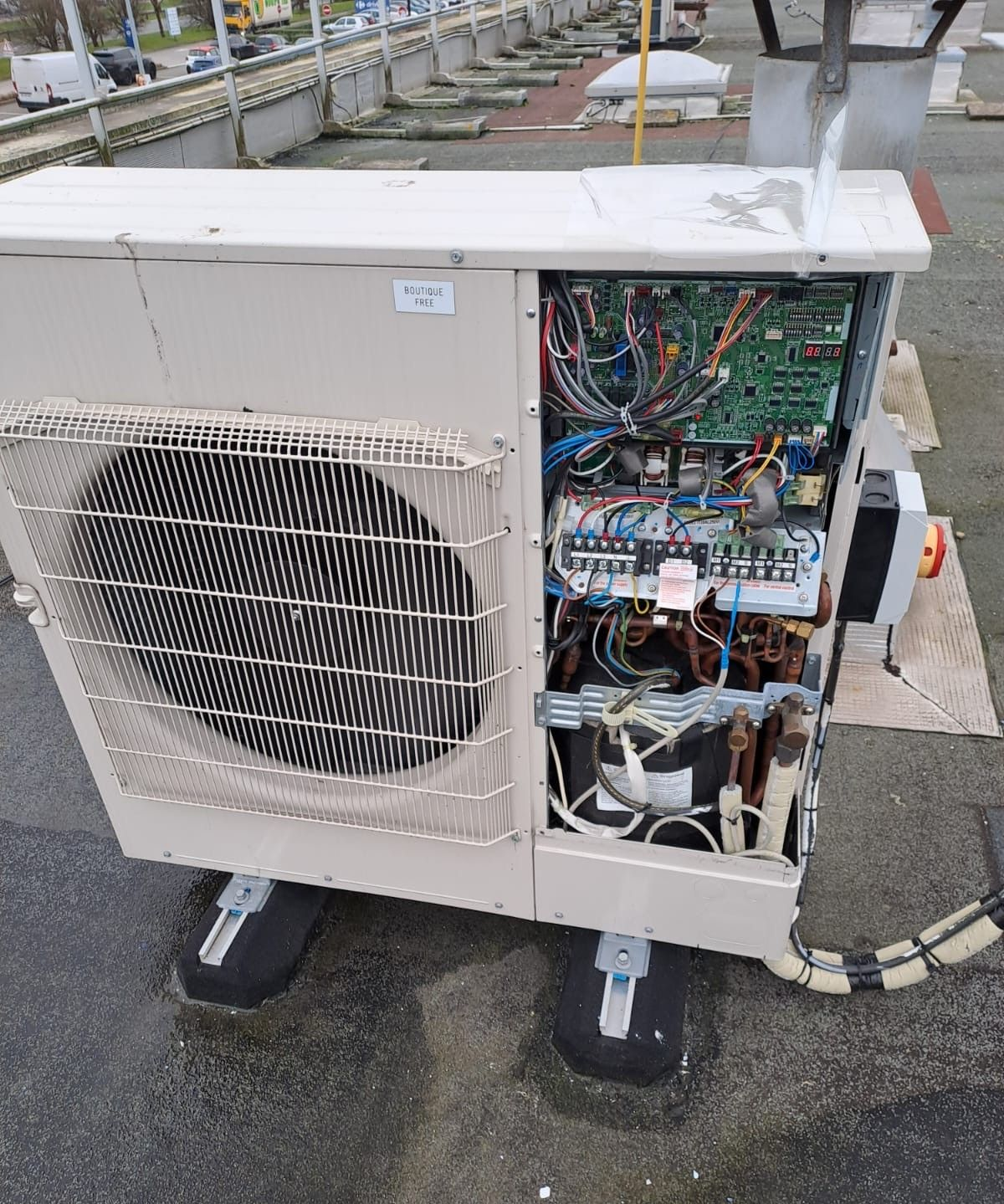 Une unité de climatisation extérieure dont le panneau latéral a été retiré, exposant les composants électriques.
