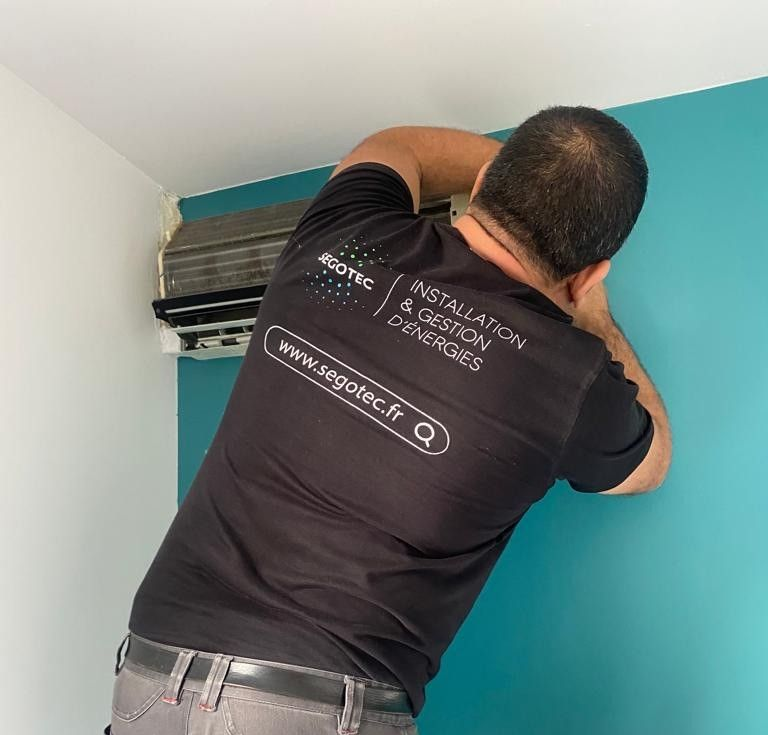 Un technicien travaille sur une unité de climatisation intérieure fixée sur un mur turquoise.
