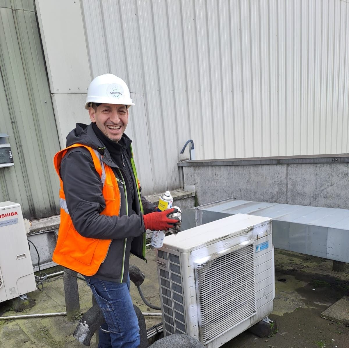 Un ouvrier tient une bombe aérosol pendant qu'il effectue l'entretien d'un climatiseur extérieur.