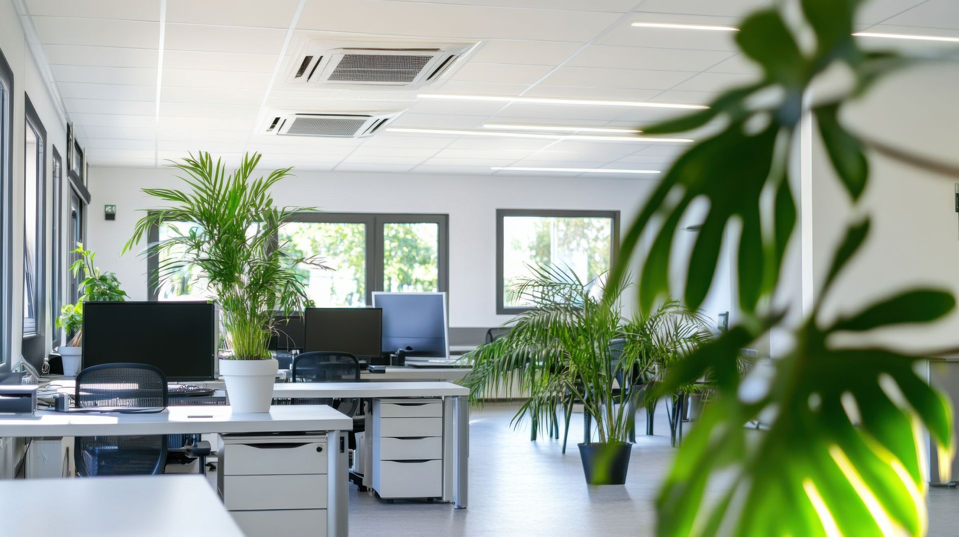 Un espace de bureau lumineux avec des bureaux, des ordinateurs et des climatiseurs.
