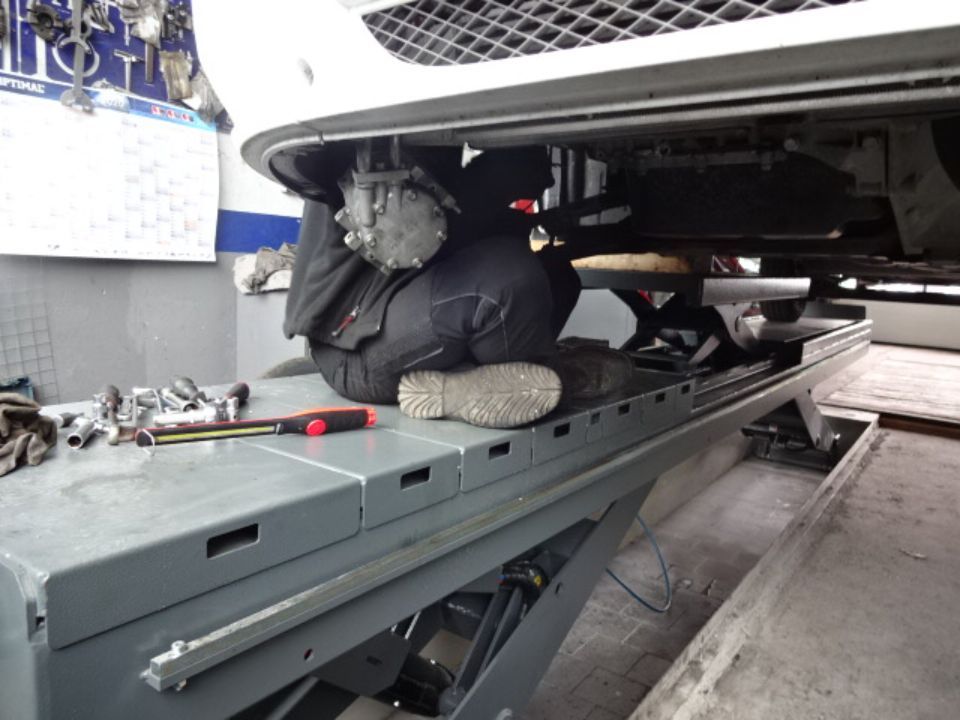 Mitarbeiter der [comapny_name] unter einem Auto das auf einer Hebebühne steht.