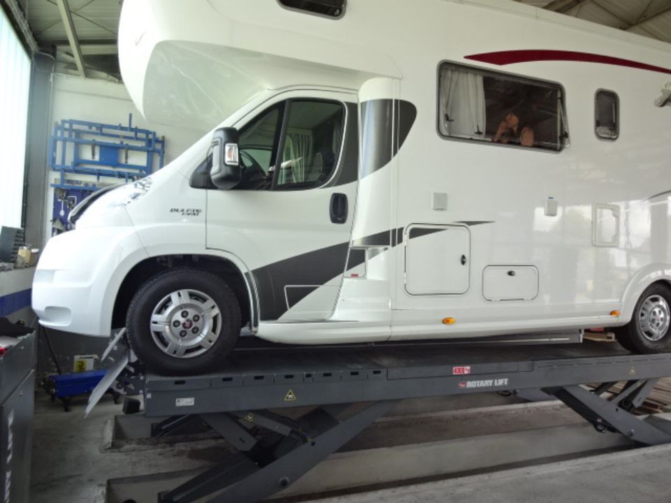 Seitenansicht von einem Wohnmobiel auf einer Hebebühne in der Werkstatt von Autohaus Raithel