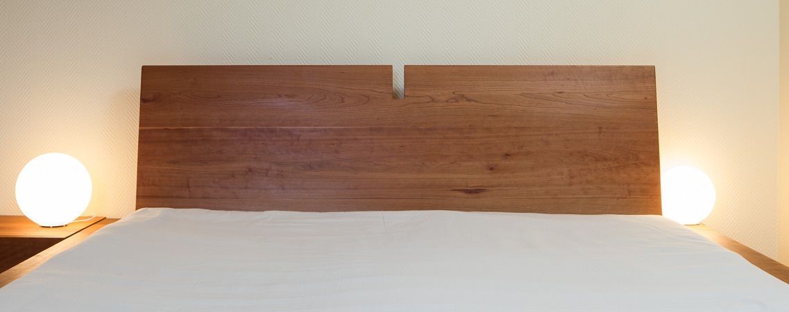 Ein Bett mit einem hölzernen Kopfteil und einer weißen Matratze in einem Schlafzimmer.