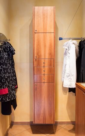 Ein Holzschrank mit Schubladen und Türen in einem Raum mit an der Wand hängender Kleidung.