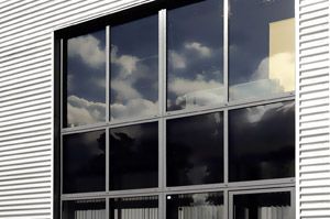 Ein großes Fenster an der Seite eines Gebäudes, in dem sich Wolken spiegeln.