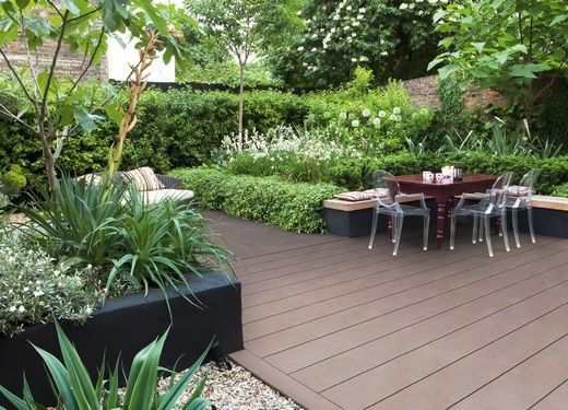 Eine Holzterrasse mit Tisch und Stühlen in einem Garten.