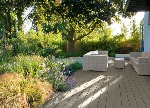 Eine Holzterrasse mit einem Sofa und Stühlen darauf in einem Garten.