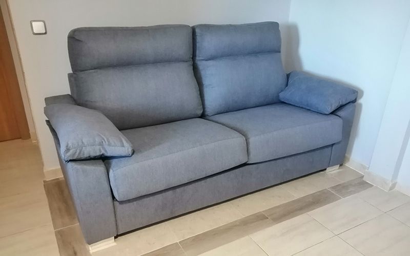 Un sofá gris está sentado sobre un piso de baldosas en una sala de estar.