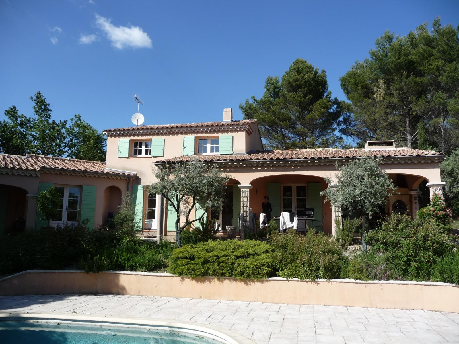Maison de style méditerranéen avec porche voûté, toit de tuiles et jardin luxuriant sous un ciel bleu azur.