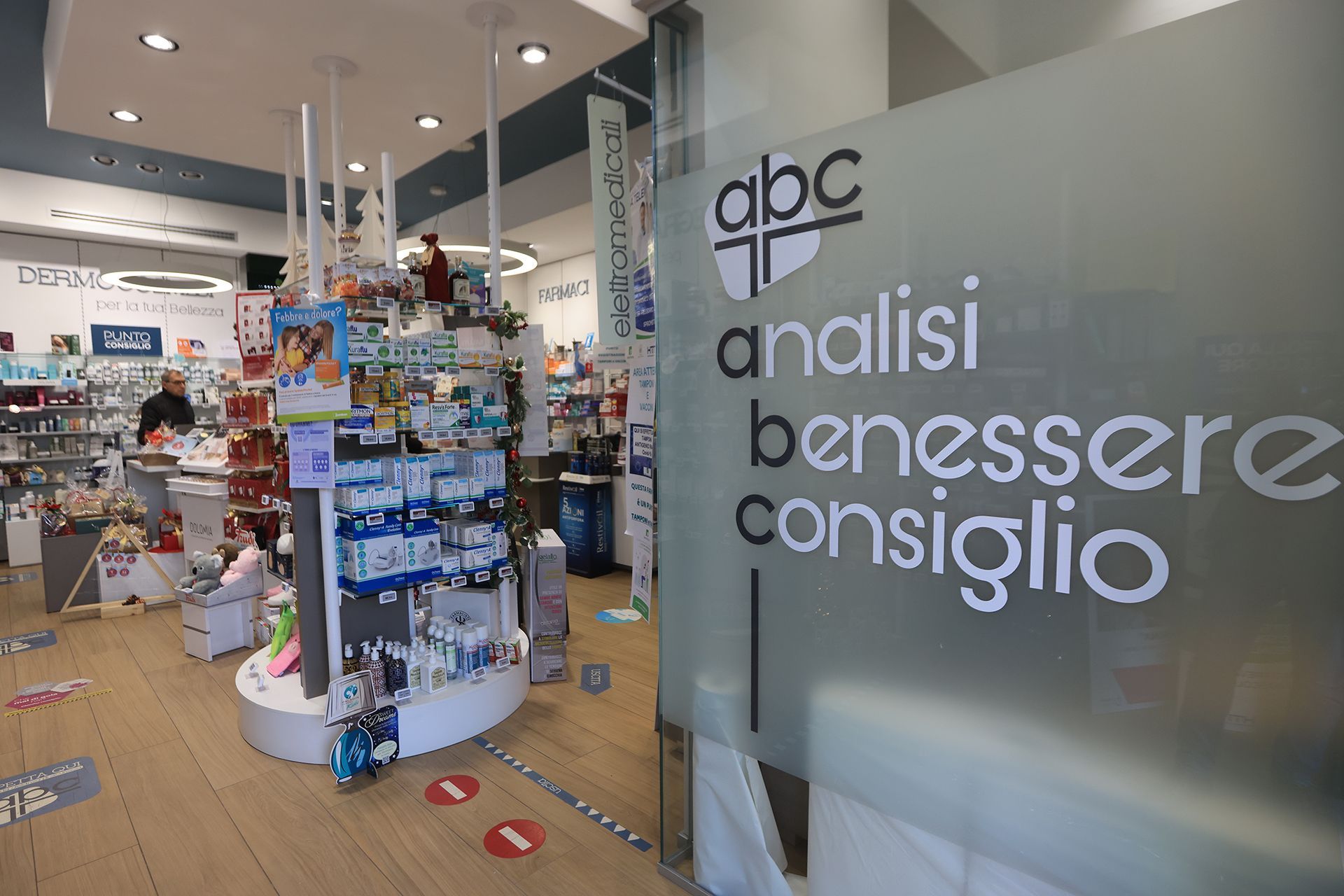 Interno della farmacia con prodotti in esposizione. Cartello con la scritta 