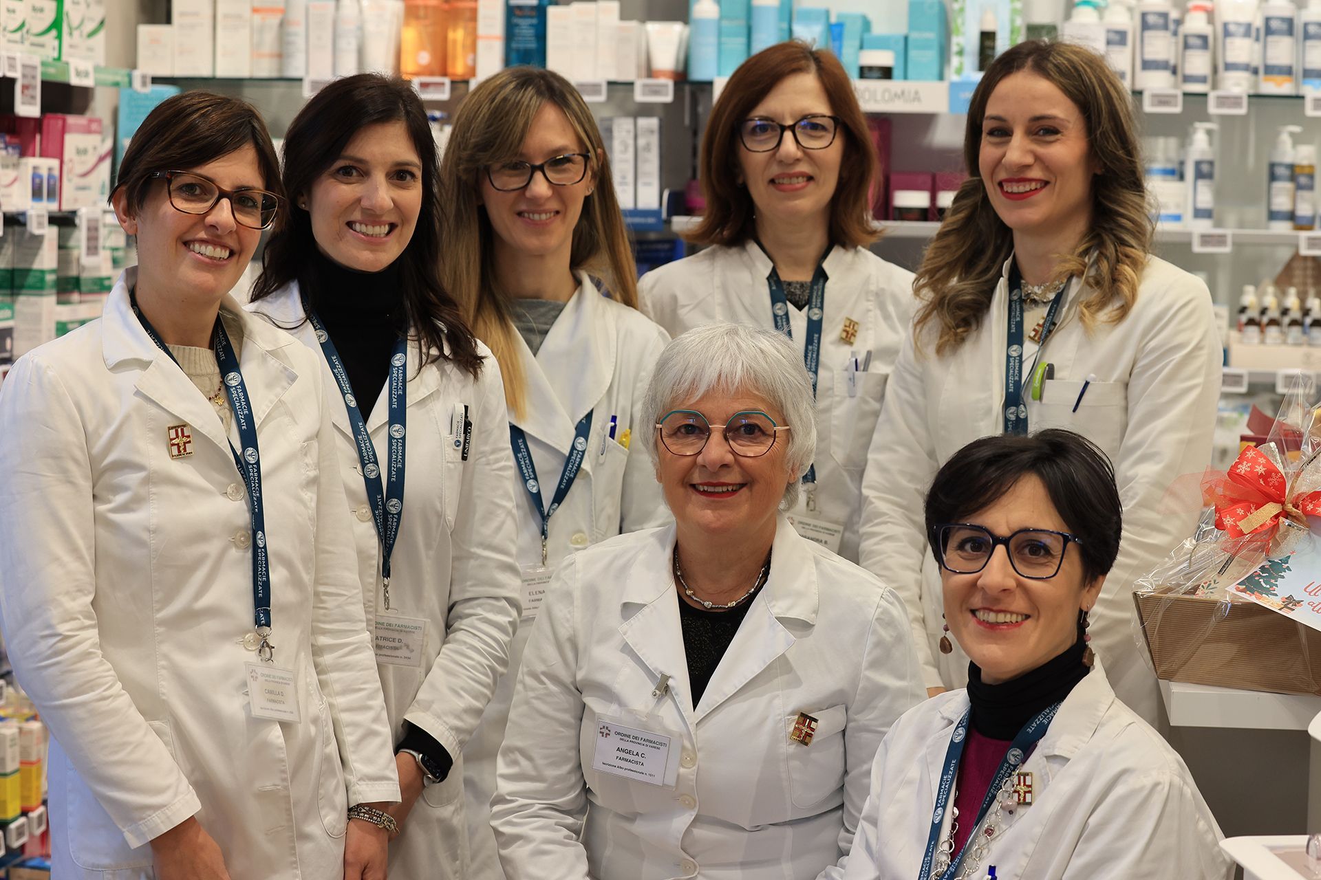 Un gruppo di sette dipendenti della farmacia in camice bianco, sorridenti in un negozio.