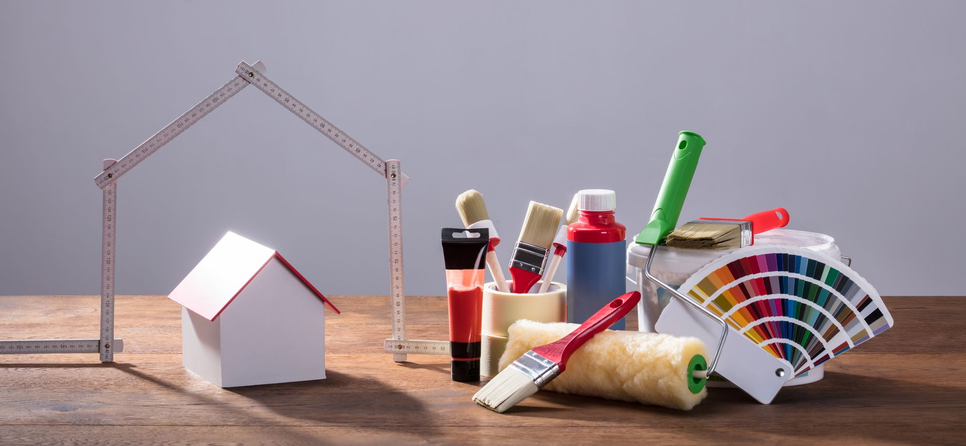 Ein Holztisch mit einem Modellhaus, Farbe, Pinseln und einem Lineal.