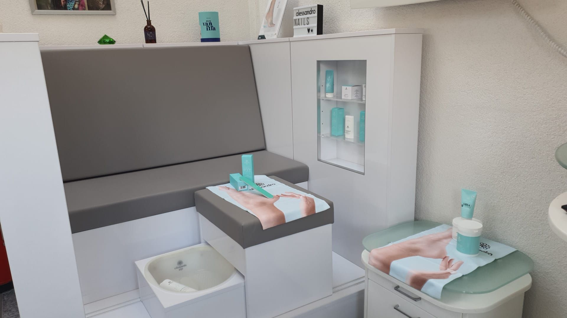 Fuß mit rot lackierten Zehennägeln, der neben violetten Orchideenblüten auf schwarzem Untergrund ruht.