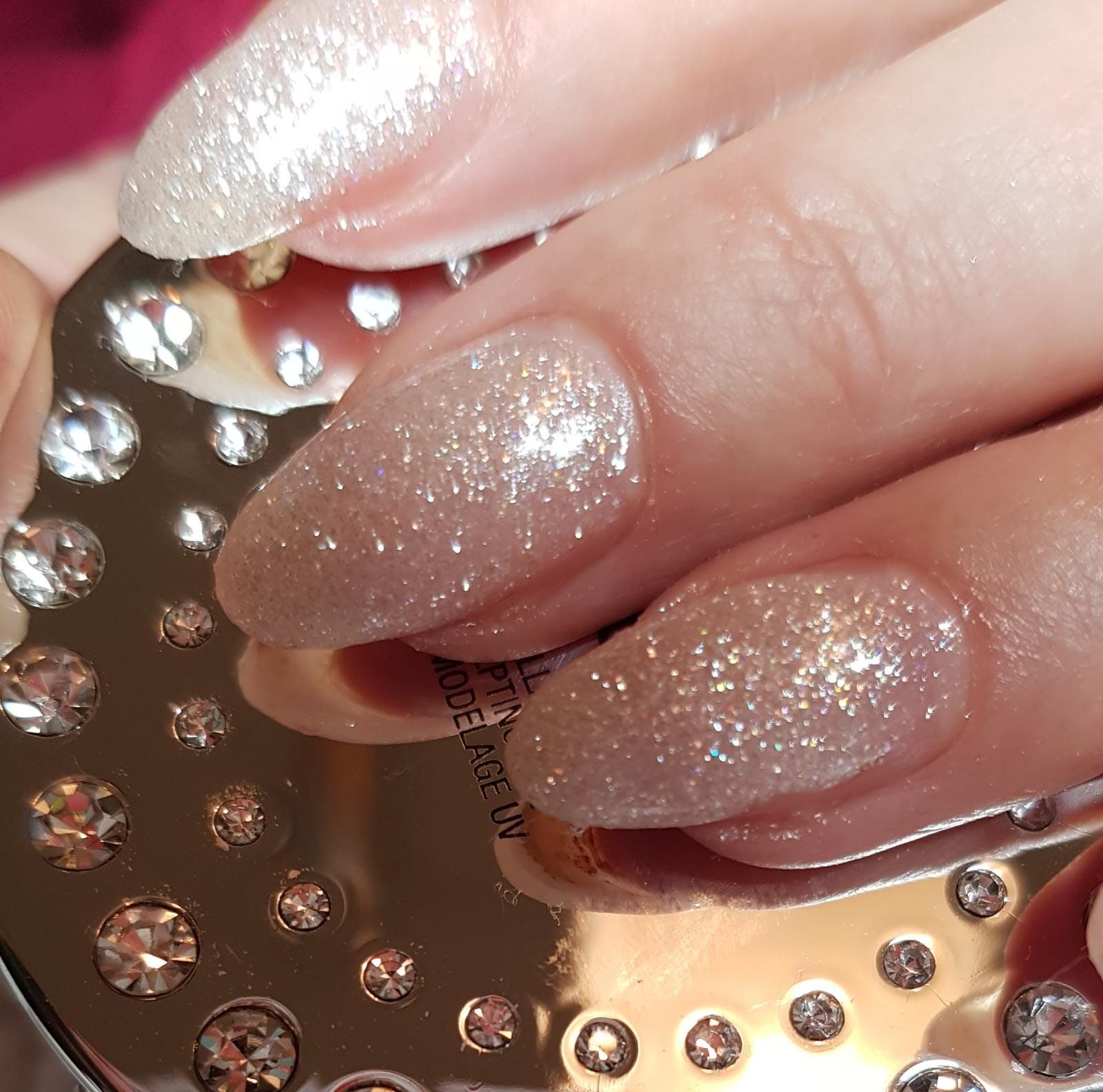 Hände mit pink- und lilaglitzerndem Nageldesign, die rosa Rosenblätter halten.