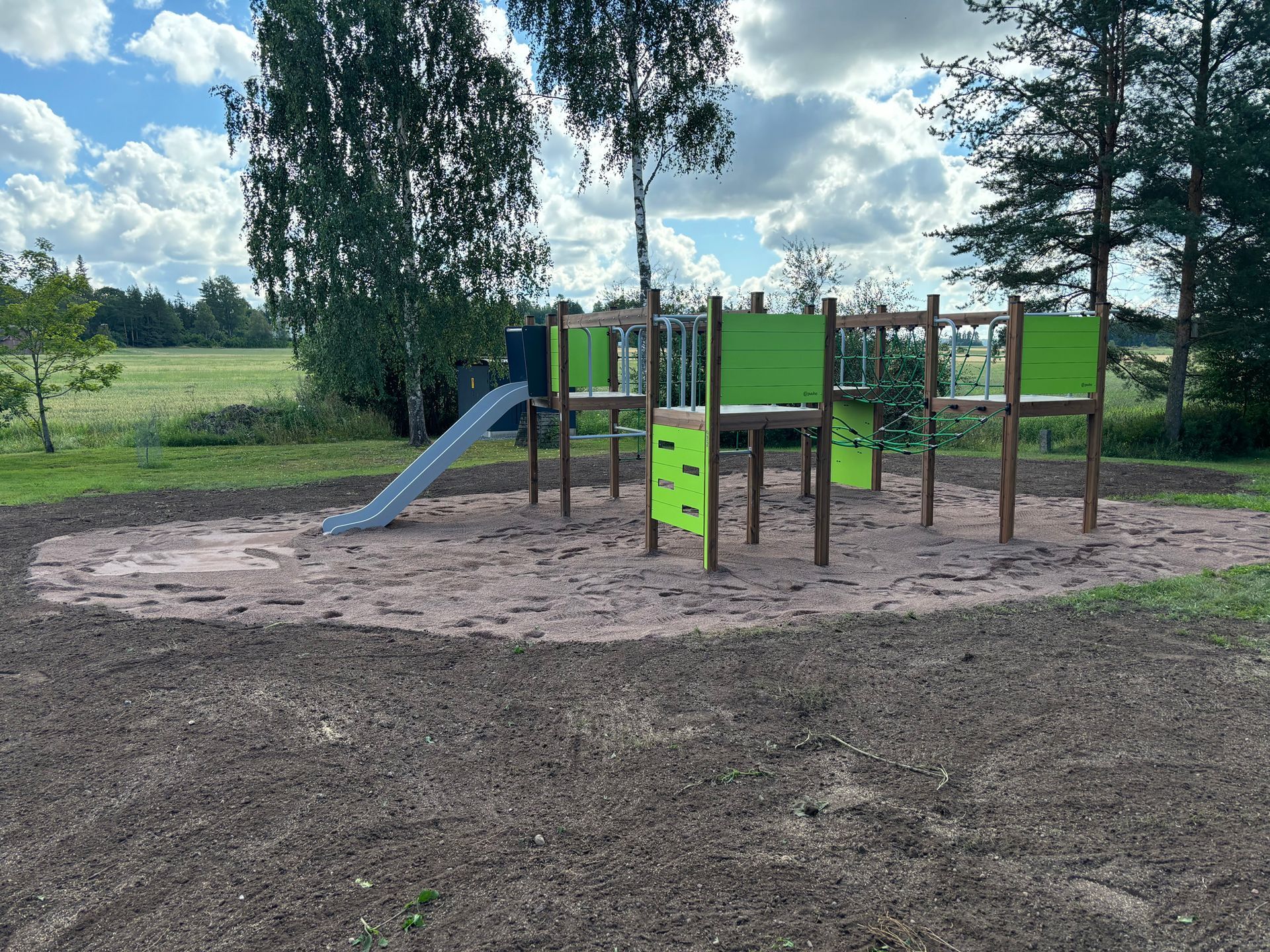 Ulkoleikkipaikka, jossa on liukumäki ja kiipeilyteline ruohokentällä pilvisen taivaan alla