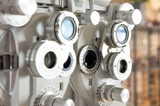 Primer plano de un foróptero plateado utilizado para exámenes oculares, que muestra múltiples lentes giratorias y diales de ajuste.