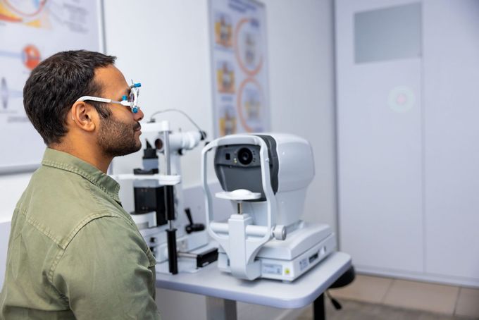 Una persona que lleva gafas de prueba está sentada en una consulta de optometría, frente a una máquina de examen ocular para una prueba de visión.