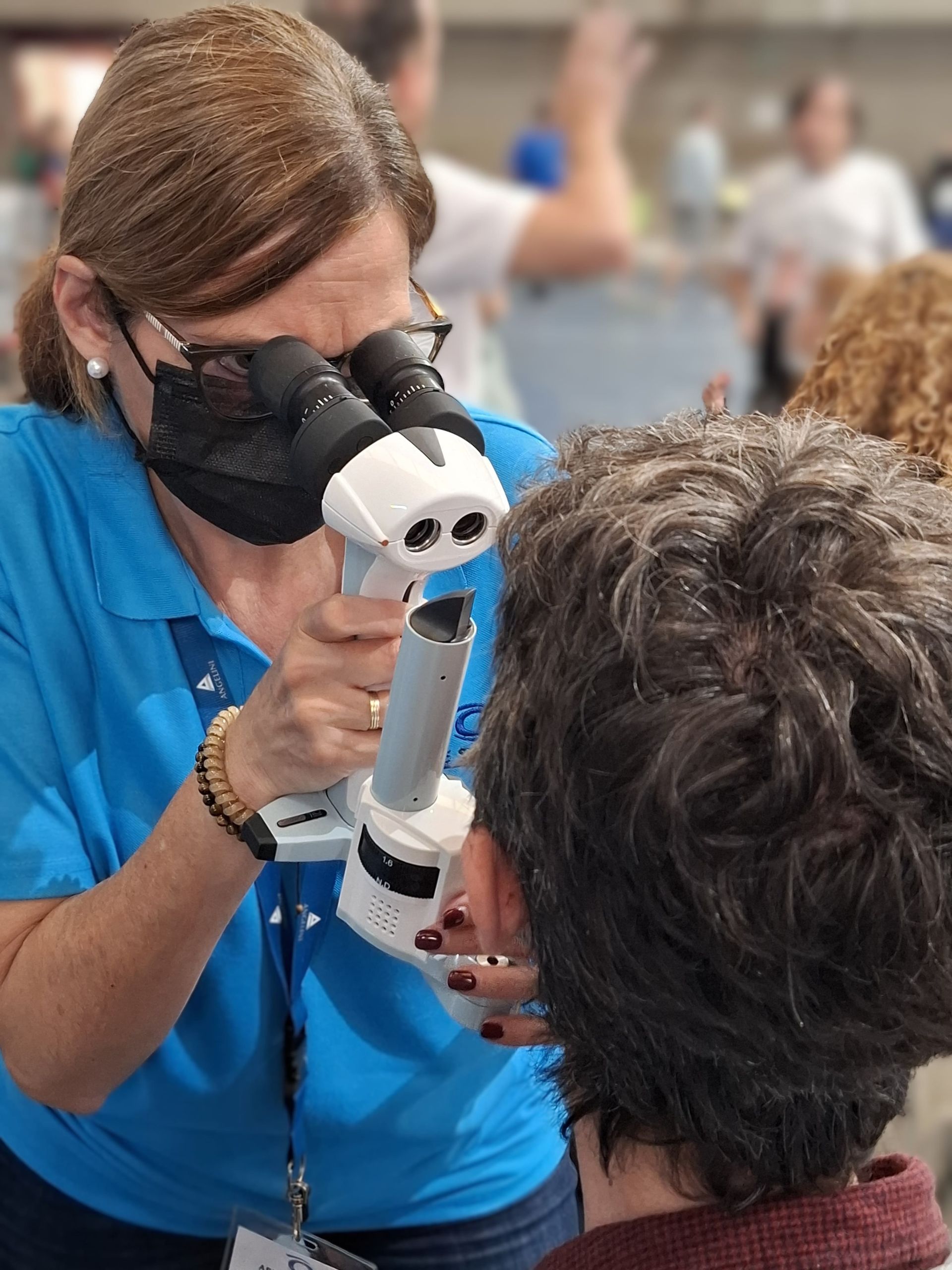 Una persona con una camisa azul utiliza una lámpara de hendidura portátil para examinar los ojos de un paciente en un entorno clínico.