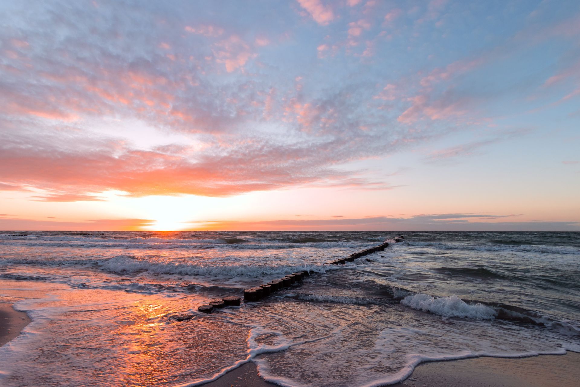 Sonnenuntergang über einem aufgewühlten Ozean mit einem schmalen Pier, der ins Wasser ragt