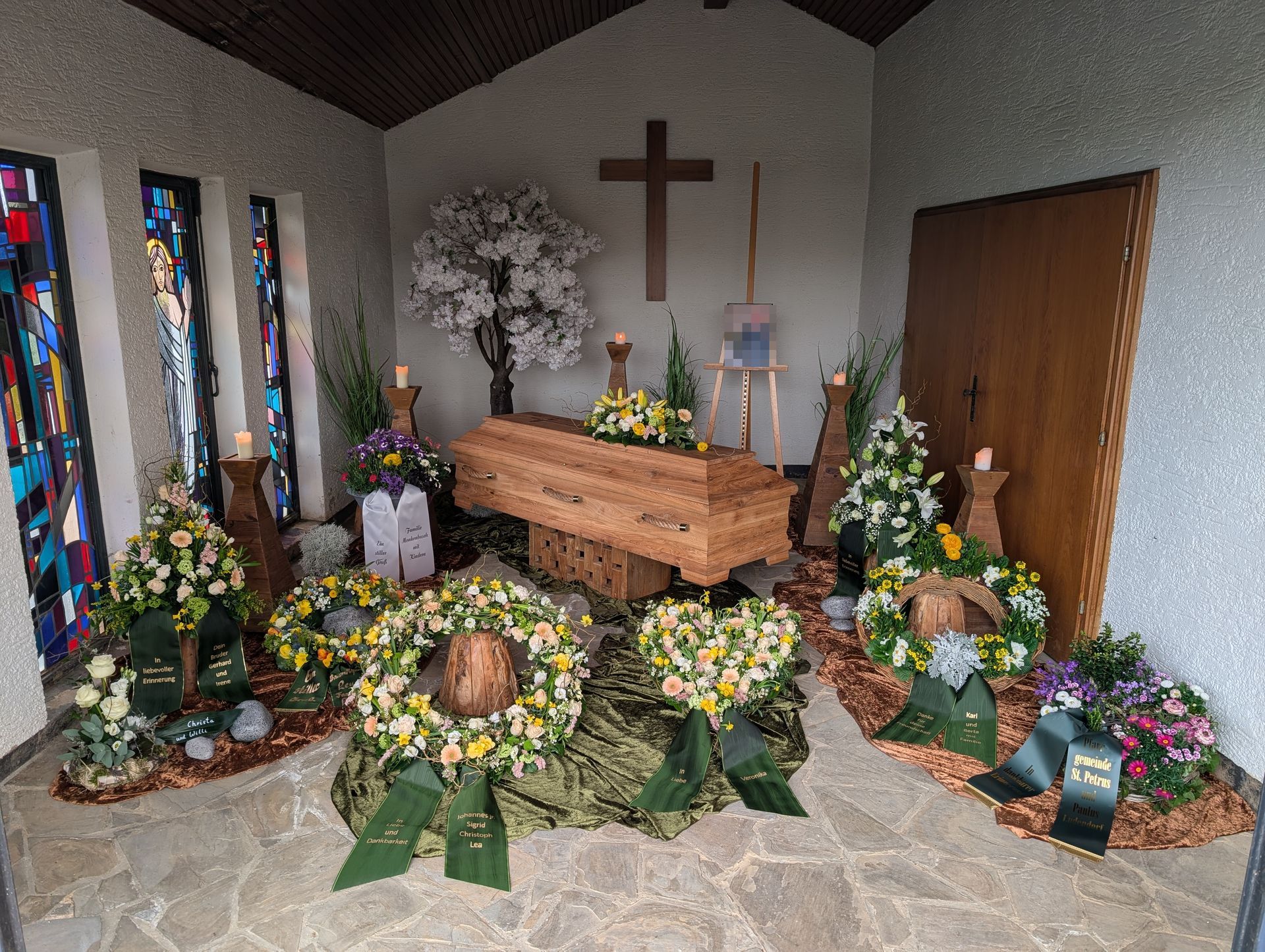 Gedenkaltar mit Blumen, Kerzen, Kreuz und Holzsarg in einer kleinen Kapelle