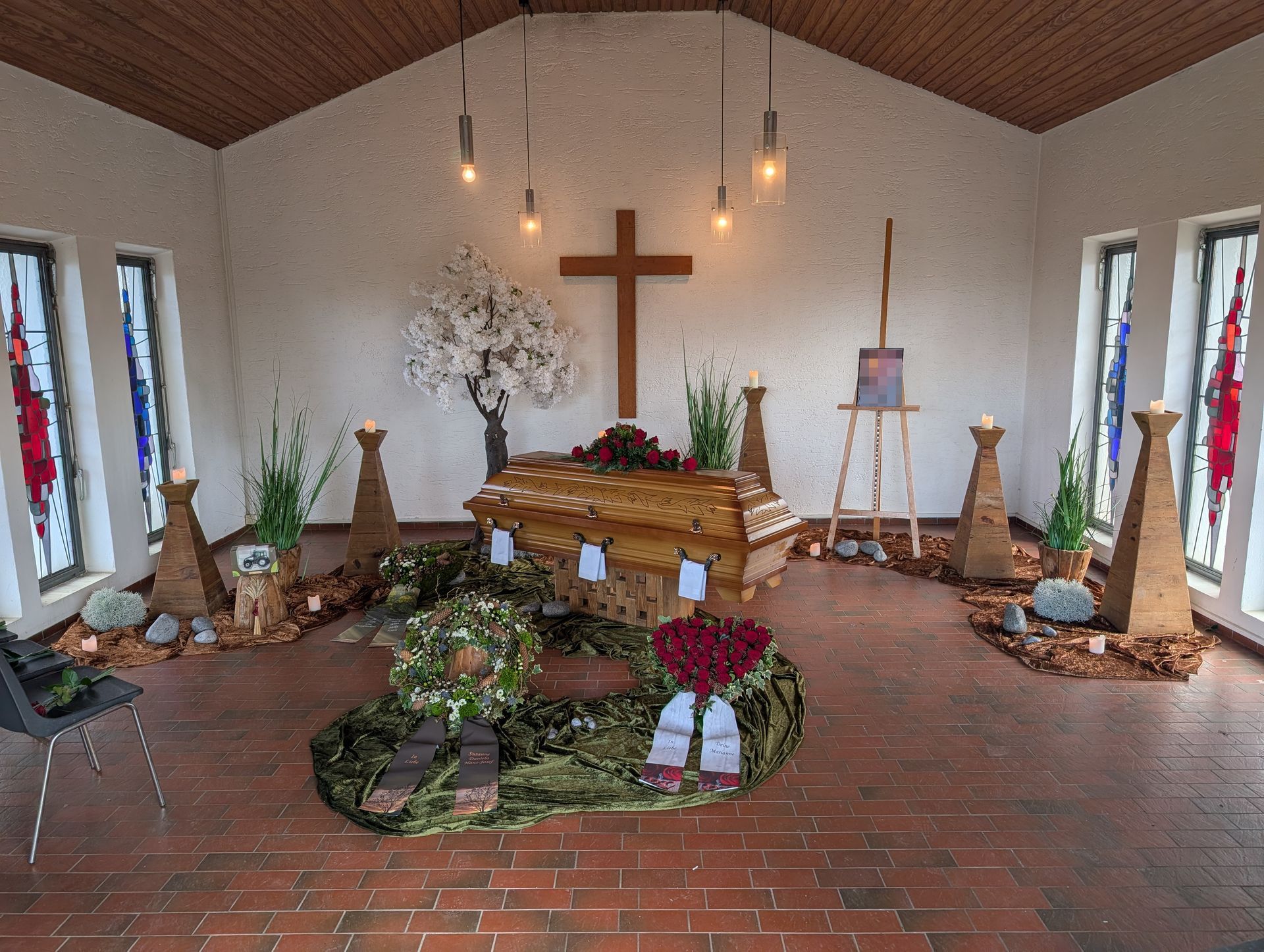 Kirchenaltar mit einem großen Kreuz, Kerzen, Blumen und Grünzeug auf einem Ziegelboden
