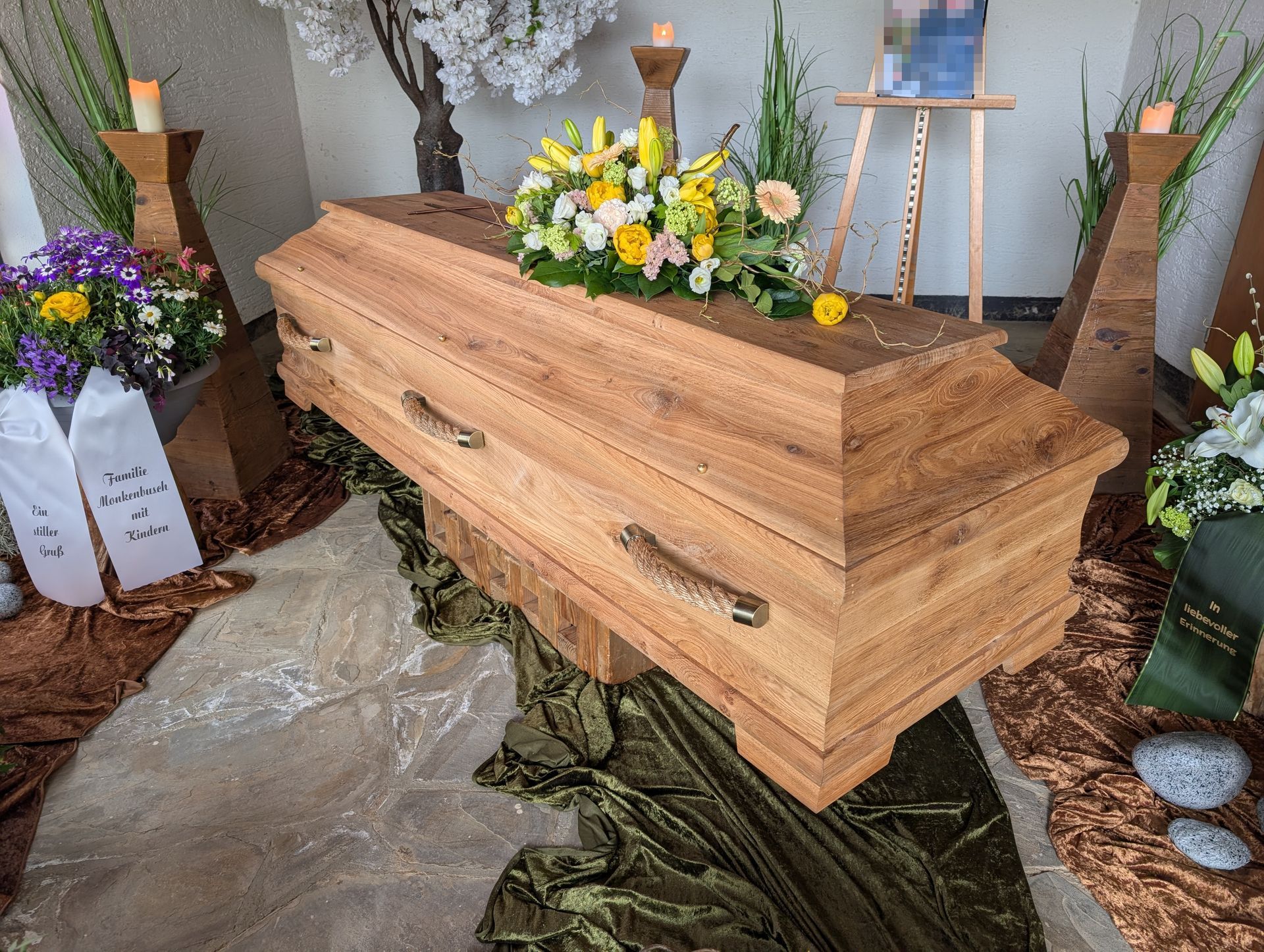 Ein Holzsarg, umgeben von Blumengestecken und Kerzen, im Innenbereich