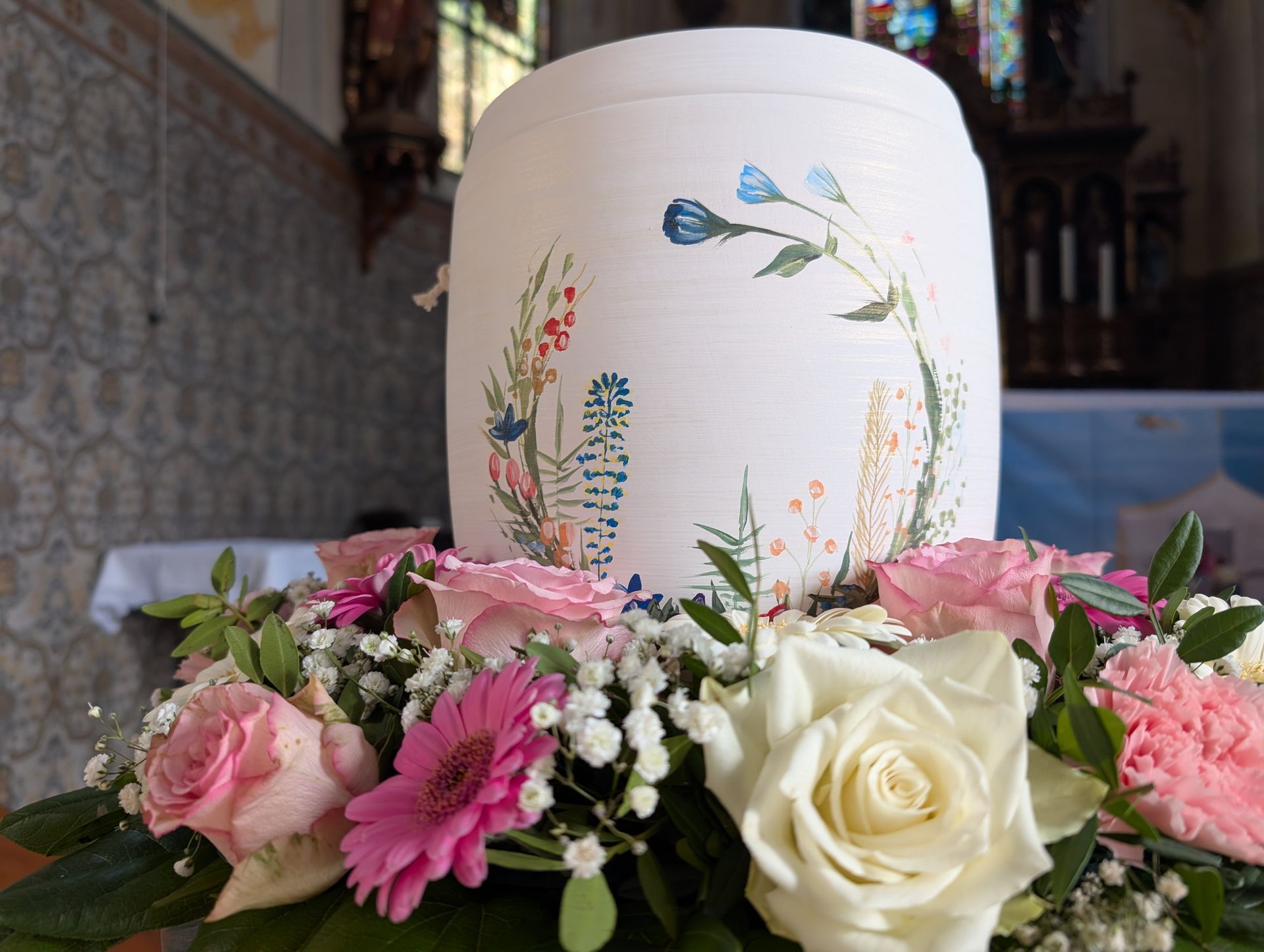 Weiße Gedenkkerze mit floralem Dekor, umgeben von rosa und weißen Blüten