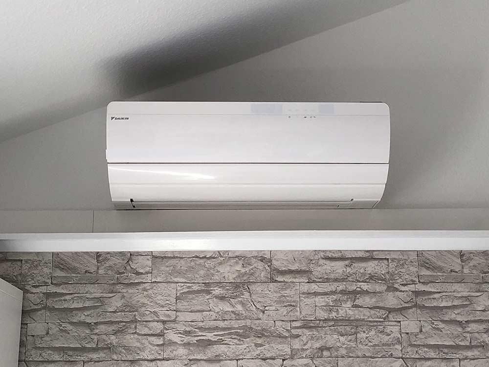 In einem Raum mit Ziegelwand hängt eine weiße Klimaanlage von der Decke.