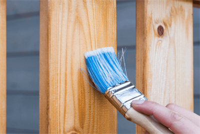 Eine Person streicht ein Holzgeländer mit einem blauen Pinsel.