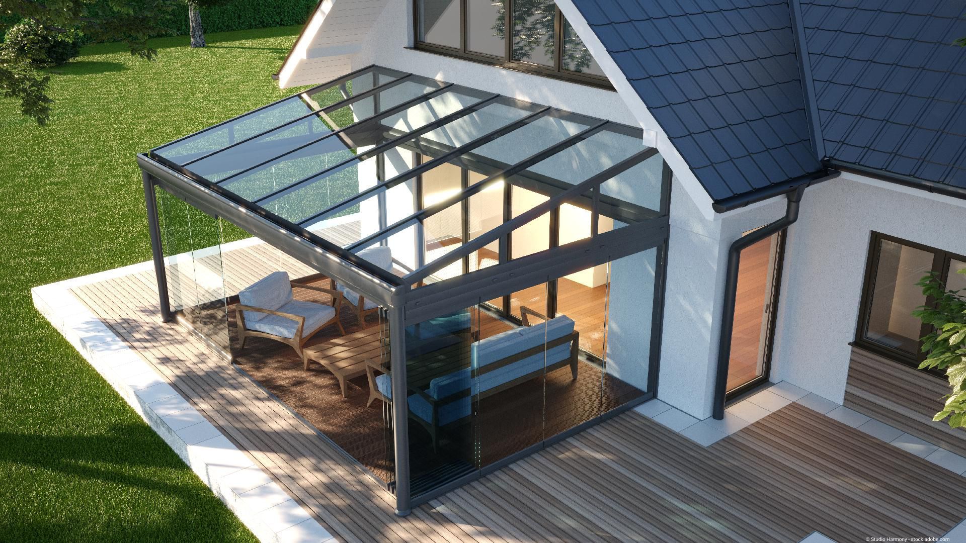 Moderner Wintergarten beziehungsweise Glasvordach aus Edelstahl und Glas an einem Haus, mit Sitzbereich auf einer Terrasse.