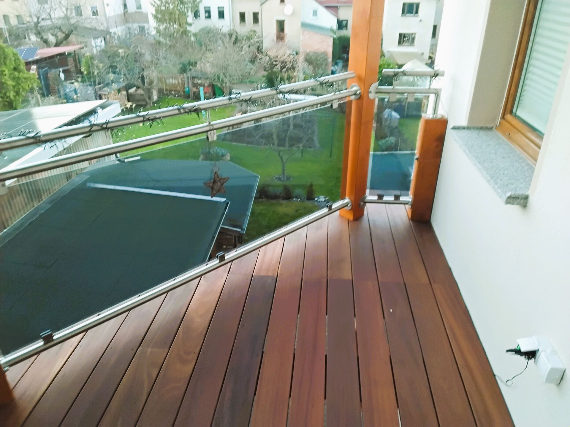 Balkon mit holzähnlichem Bodenbelag und Edelstahlgeländer aus Innenperspektive